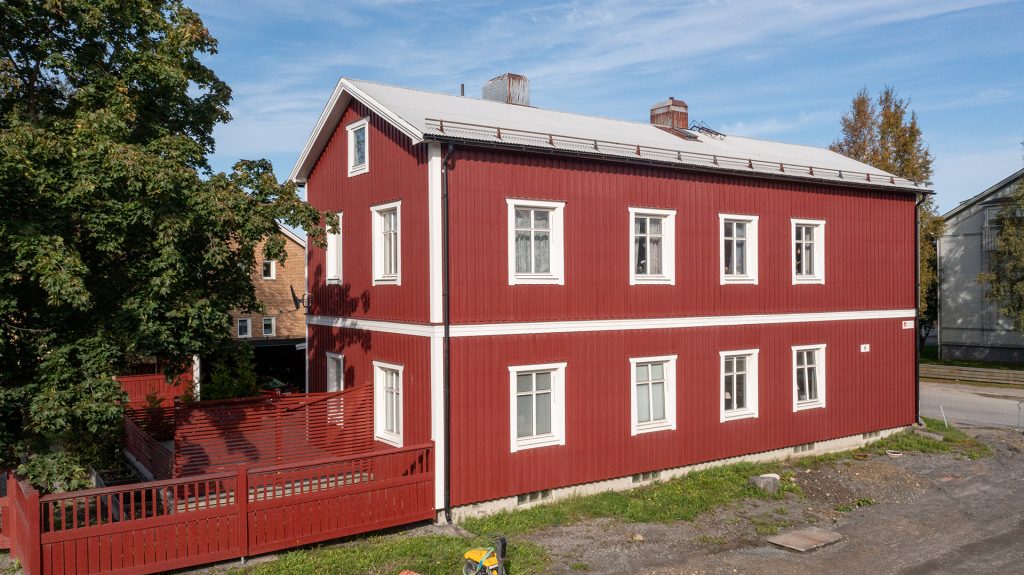 Ett rött lägenhetshus med vita knutar på Brogatan 8 i Skellefteå, under sommaren