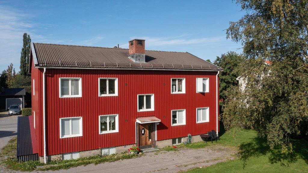 Ett rött lägenhetshus med vita knutar på Plangatan 25 i Skellefteå, under sommaren